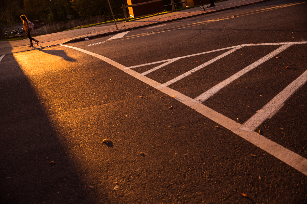 creative photo of lauren walking on the other side of the road in the sunset with the crosswalk lines leading to her for this arts quest photographer image taken by rhinehart photography