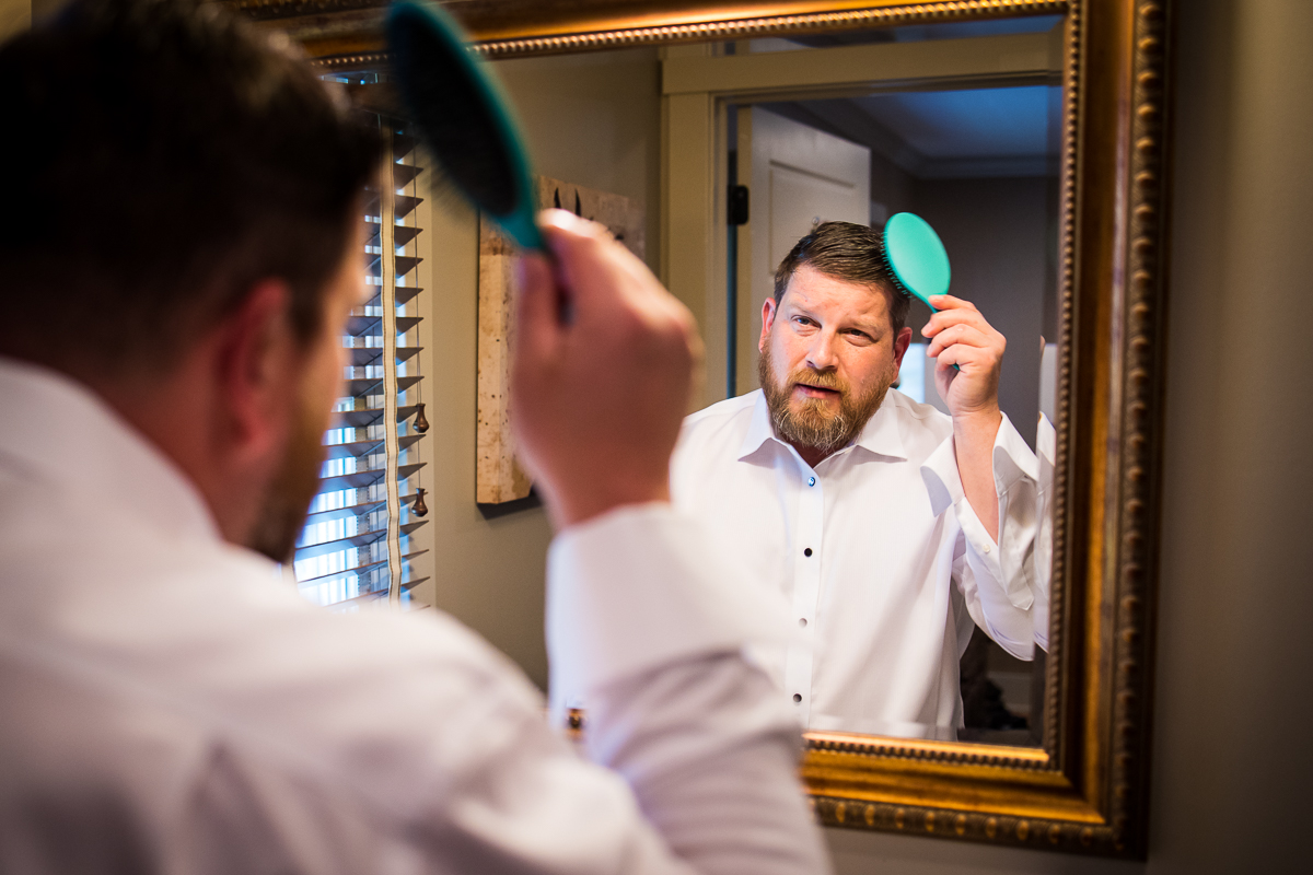 unique image of the groom getting ready and brushing his hair in the mirror before his linwood estate wedding ceremony
