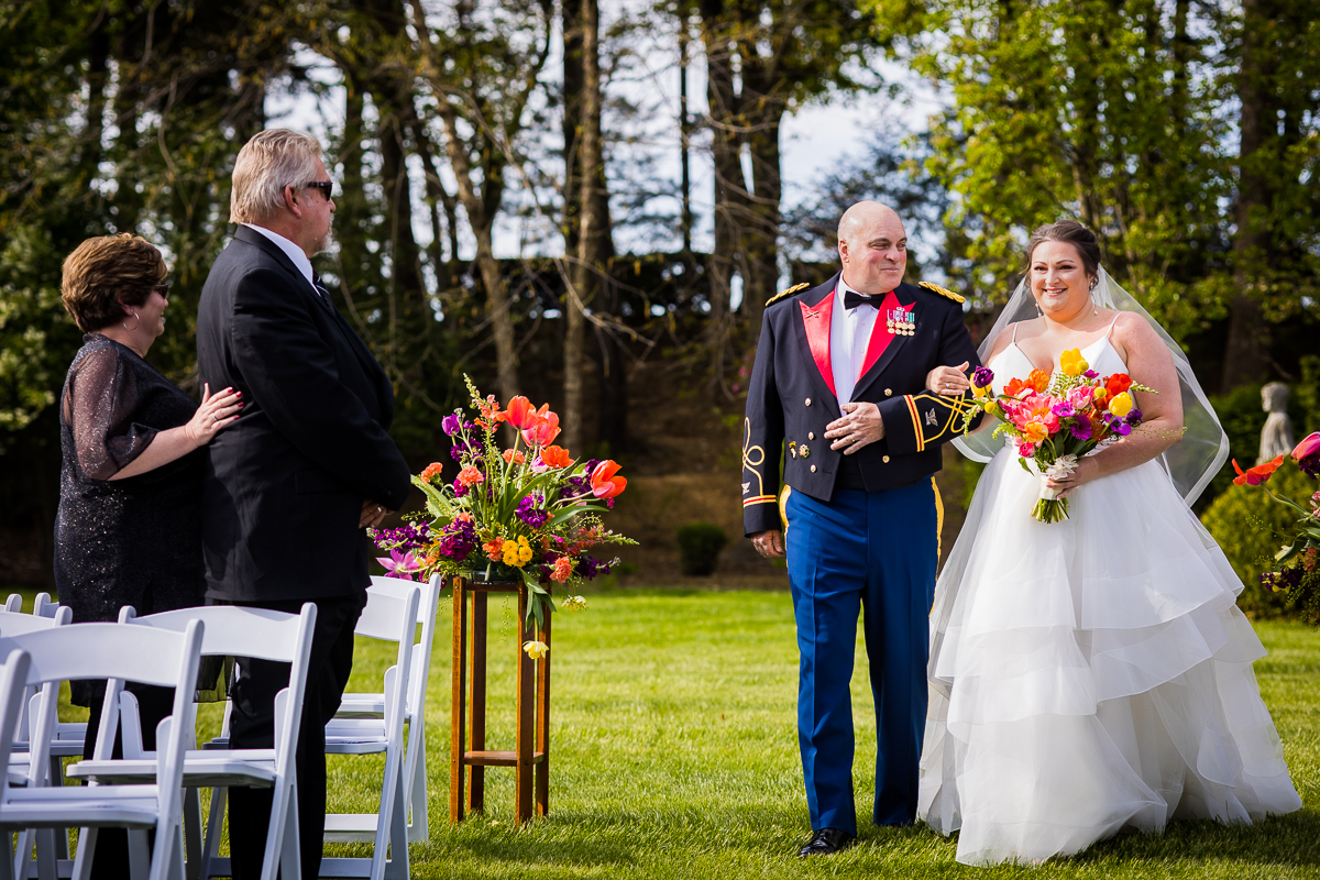 colorful and vibrant image of the bride and her father walking down the aisle together holding arms while the dad smiles looking at her during this linwood estate wedding in carlisle pa