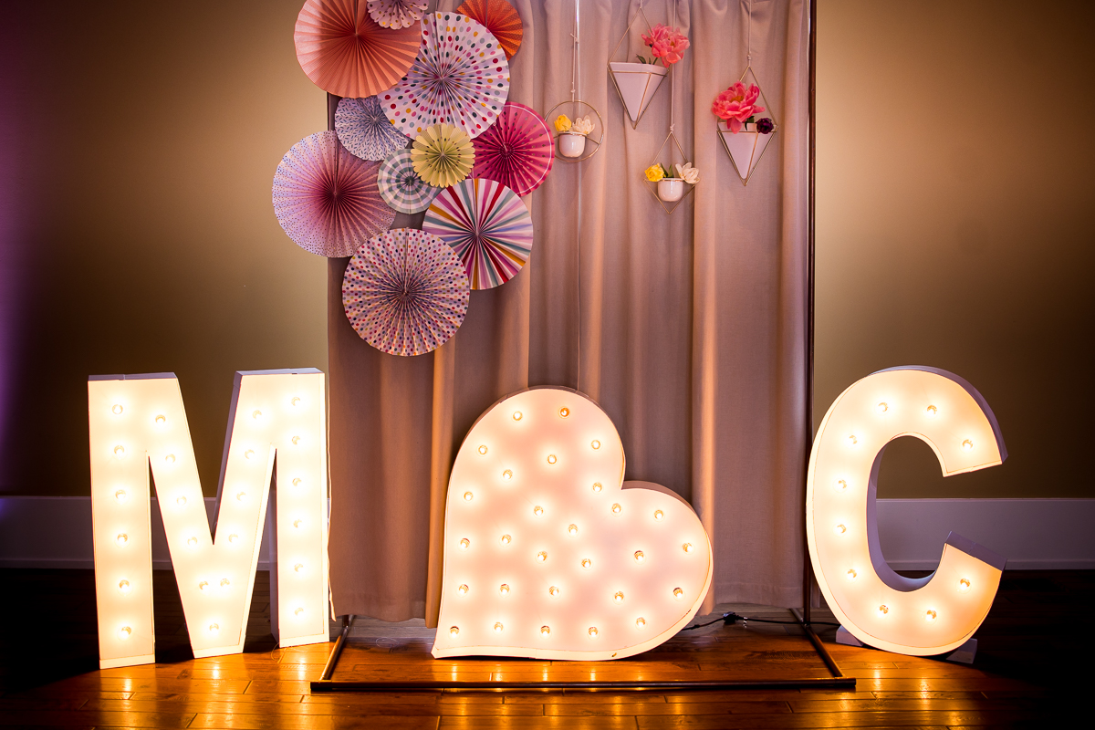 image of the couples initials lit up with lights and colorful paper fans behind it for this wedding reception