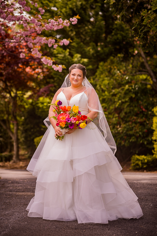 Colorful, traditional portrait of the bride smiling at the camera holding her vibrant bouquet before her linwood estate wedding ceremony