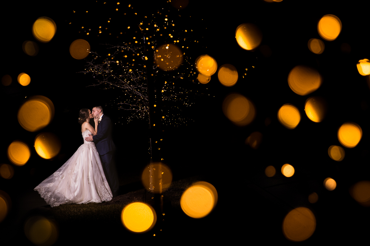creative, unique photo taken by Lisa Rhinehart, central PA wedding photographer, of the couple kissing under a golden lit tree with the light reflections for this liberty mountain resort wedding