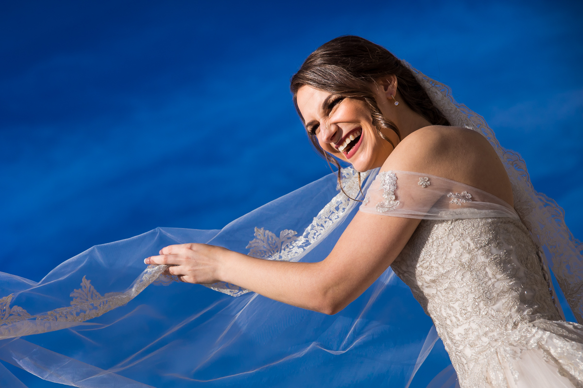 vibrant blue photo of the bride smiling holding her veil in her wedding dress for this liberty mountain wedding with central pa photographer, Lisa Rhinehart