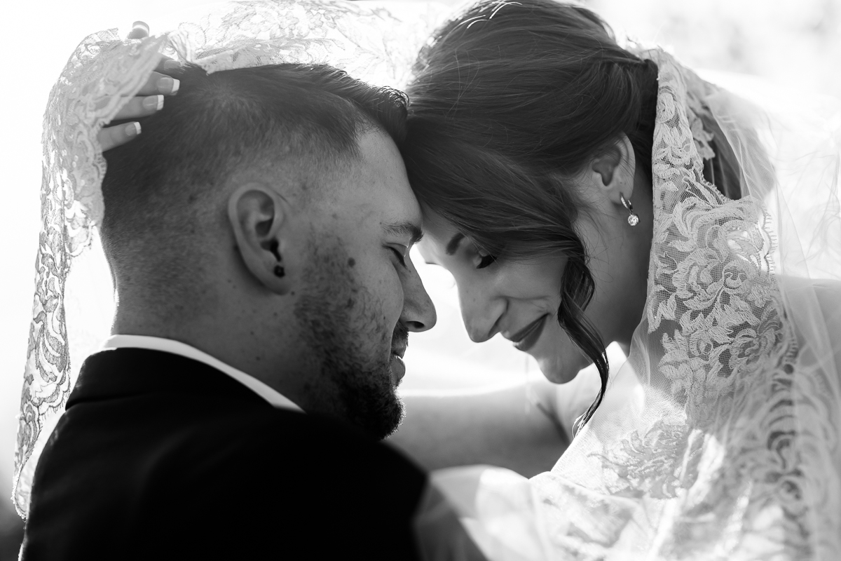 Black and white image of the bride and groom underneath the bride's veil with their heads together smiling at each other before their Liberty Mountain wedding ceremony