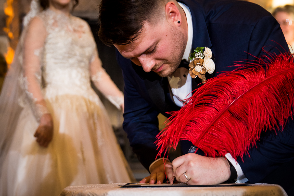 image of the groom signing papers with a giant red feathered pen during their wedding ceremony at liberty mountain resort