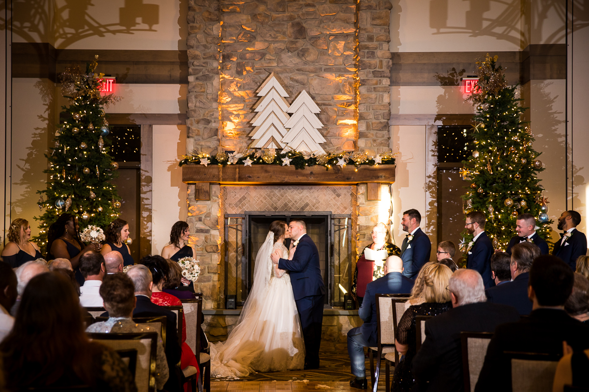 image of the bride and groom kissing one another during their ceremony with Christmas trees and decorations in the background for this liberty mountain resort wedding 