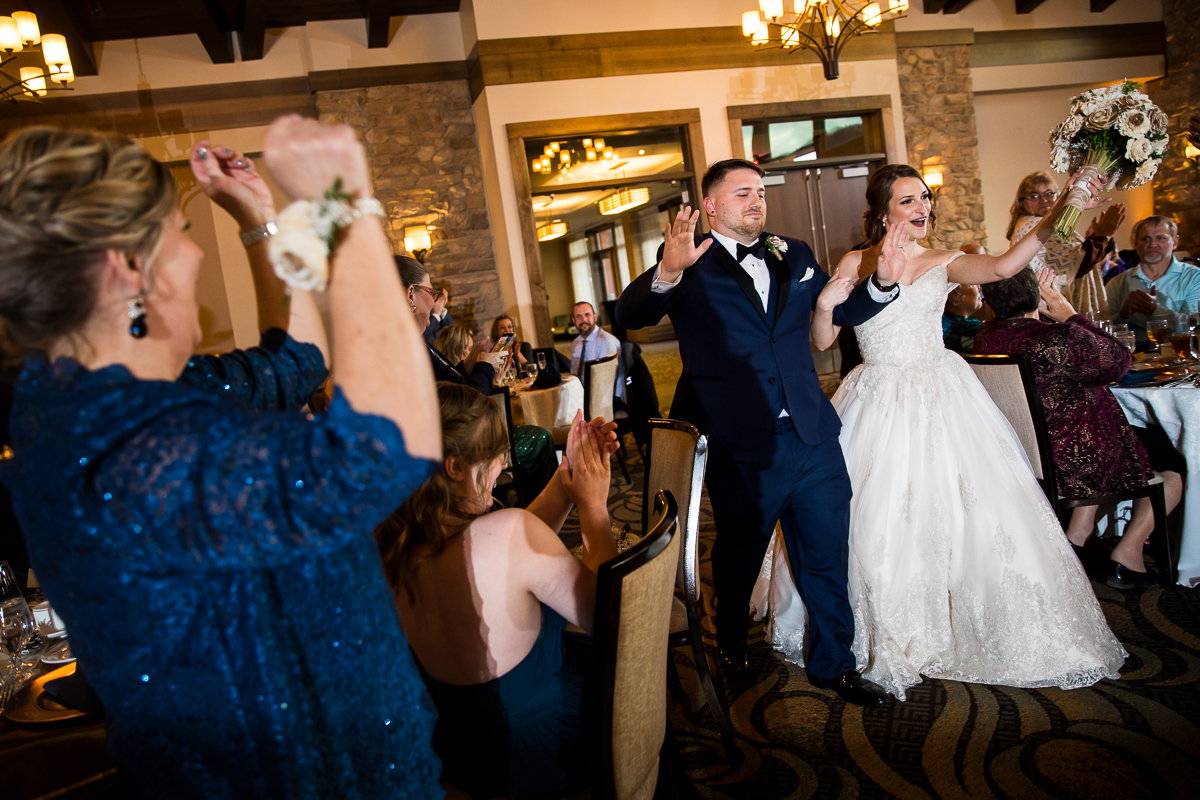 image of the bride and groom walking into their wedding reception with guests cheering, clapping and dancing