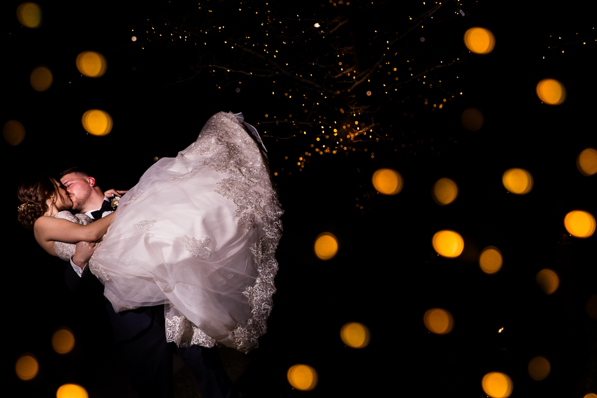 Unique, creative photography done by creative wedding photographer lisa rhinehart of the groom holding the bride kissing her with gold reflections of the lights in the tree surrounding them at this liberty mountain resort wedding 