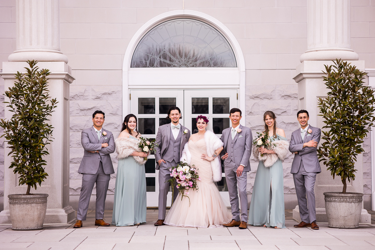 light, traditional portrait of the wedding party standing outside in front of a big door and window for this Palace at Somerset Park Wedding