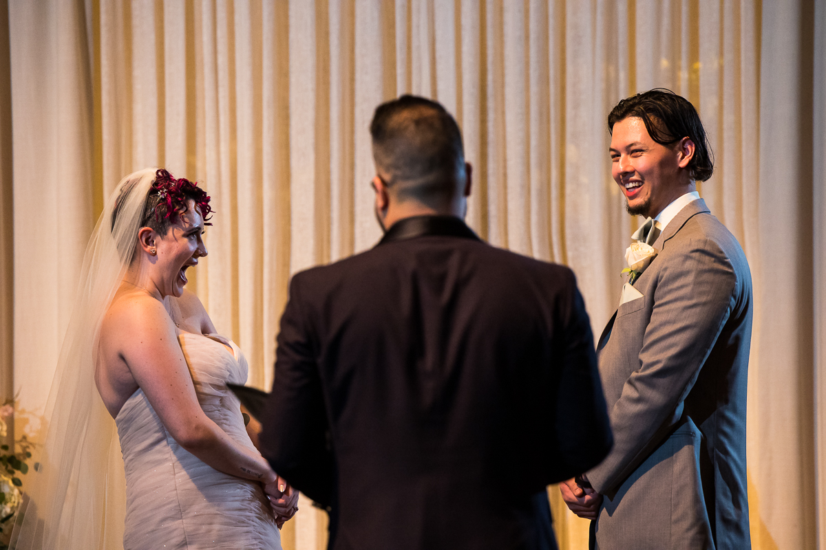 image of the bride and groom smiling as they stand together at the end of the aisle during their wedding ceremony inside of the palace at somerset park 