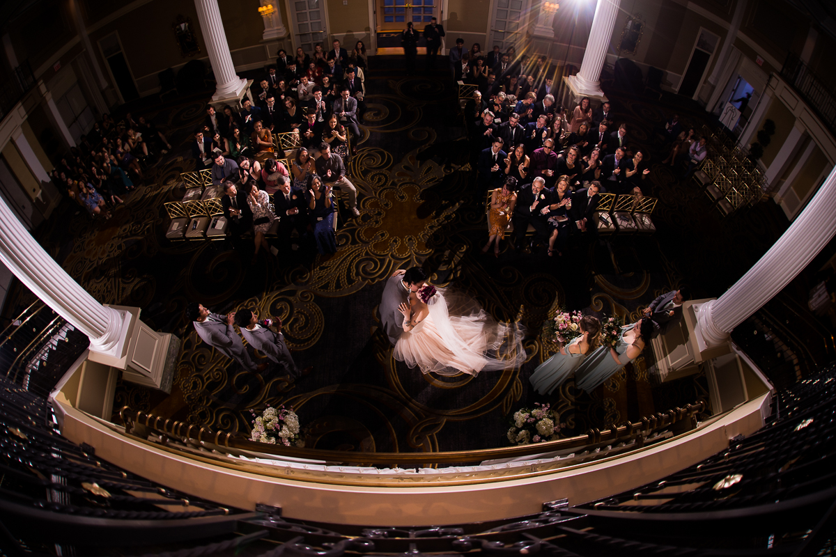 Palace at Somerset Park Wedding photographer, lisa rhinehart, captures this wide angle image of the bride and groom kissing during their ceremony with all of their guests and venue in the background with them 