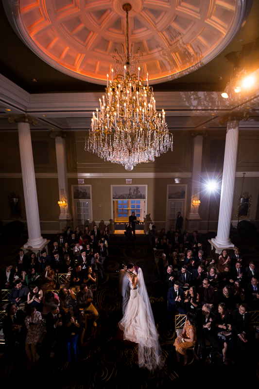 creative, unique image of the bride and groom kissing in the middle of the aisle with the chandelier above them during their Palace at Somerset Park Wedding