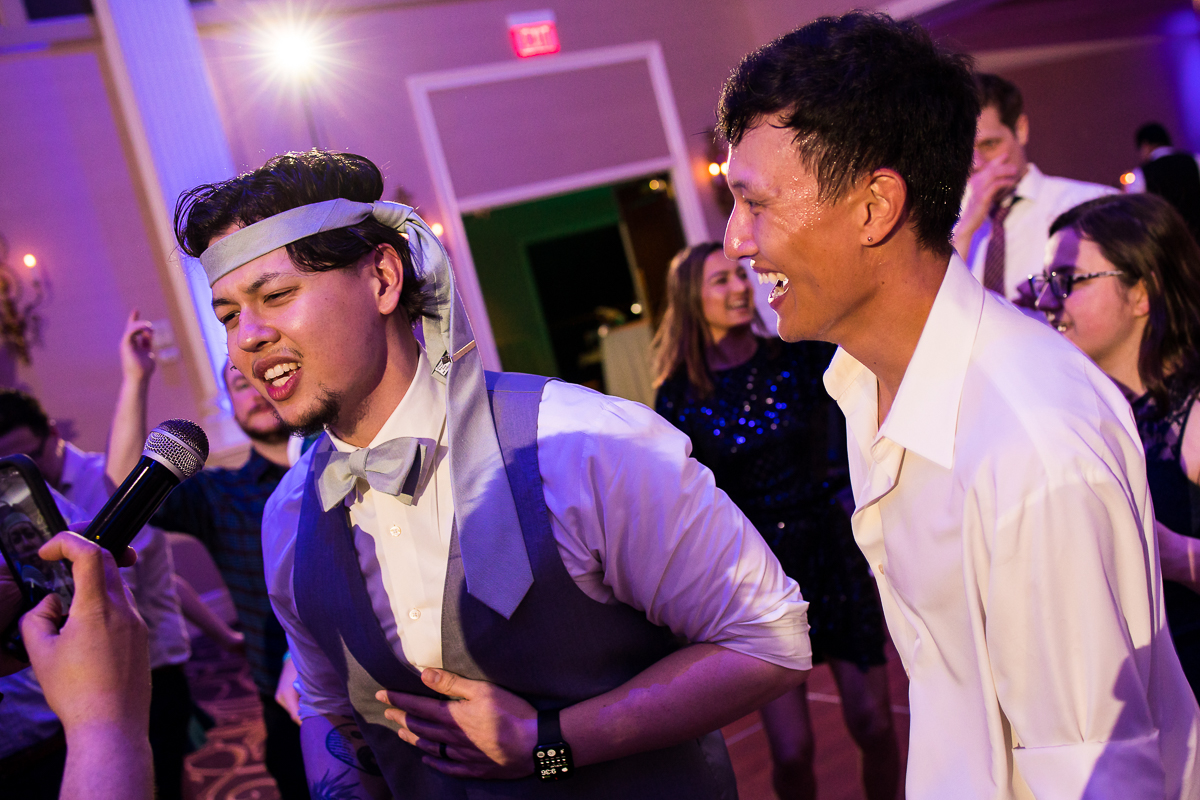 the palace wedding photographer, lisa rhinehart, captures the groom with his tie on his head as he sings and dances into the microphone during his wedding reception 