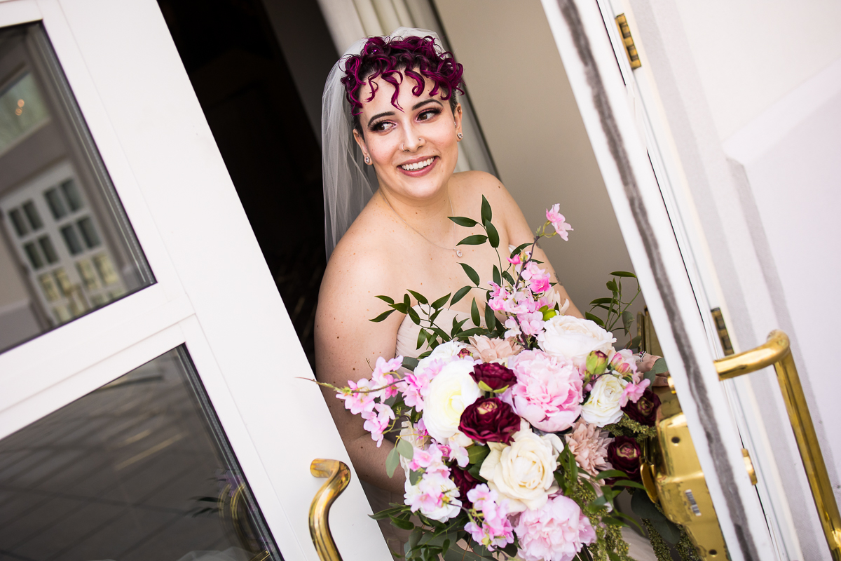 light, bright, vibrant image of the bride coming out of the door holding her vibrant colorful silk flowers during her first look for this Palace at Somerset Park Wedding