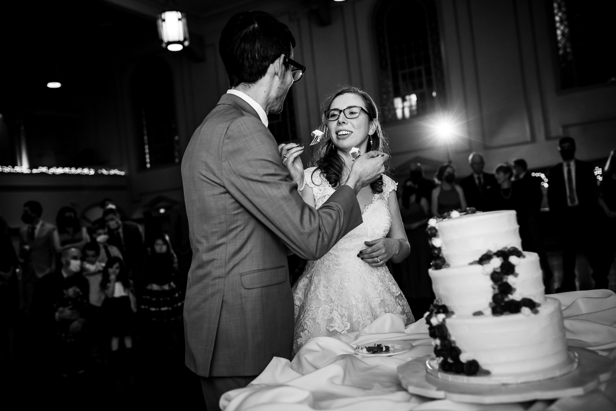 Black and white image of the bride and groom cutting and eating their cake together during their Rochester NY Wedding reception