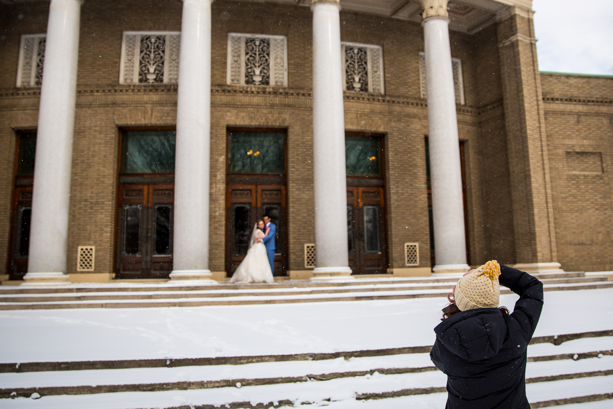 behind the scenes photo of photographer lisa rhinehart capturing the couple outside of the building before their wedding in NY