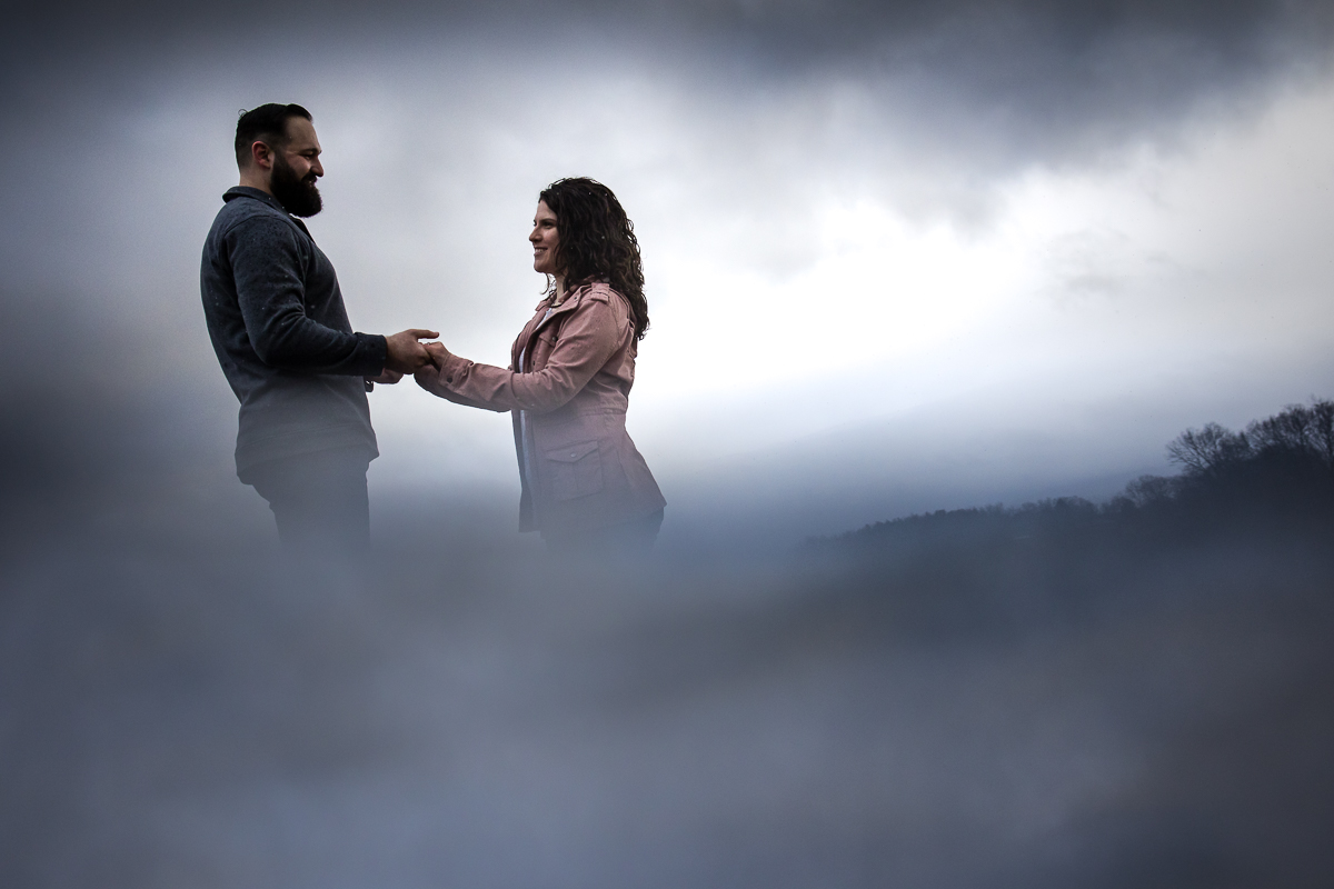 image of the couple holding hands and looking at one another as they are surrounded by mist and fog during their session at misty meadows farm creamery 