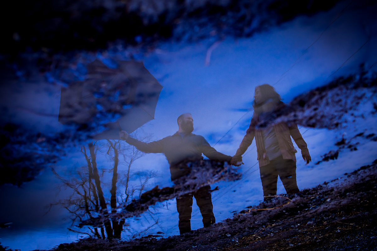unique creative vibrant image of the couple holding hands and their reflections are captured in a rain puddle during their Rainy Pen Mar Engagement session