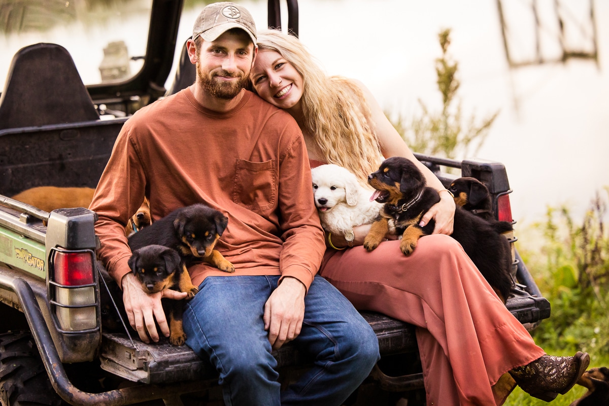 unique image of the couple sitting on their gator with all the puppies around them for this Dog Engagement Session shoot