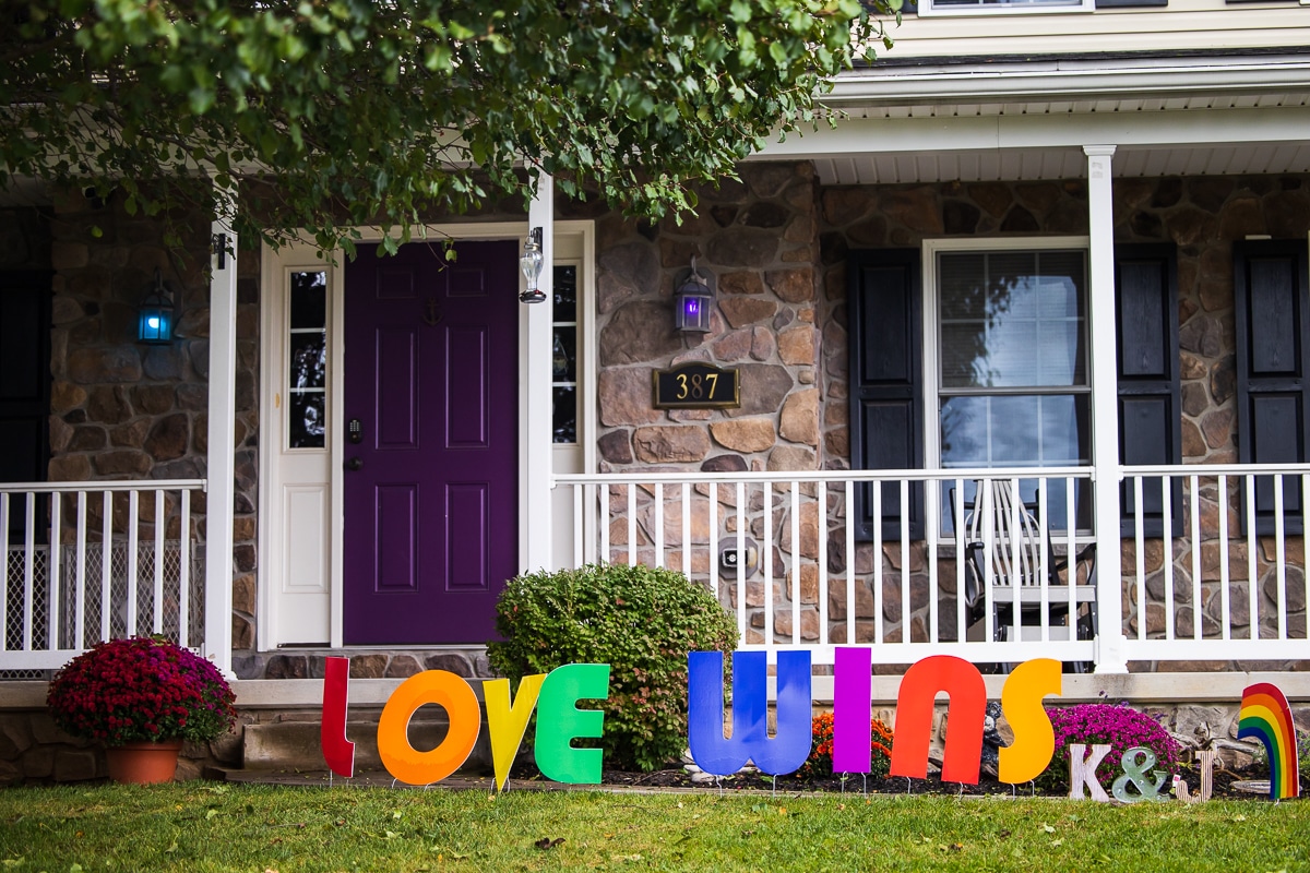 LGBTQ+ Wedding Photographer, Lisa Rhinehart captured the front of this couple's venue with colorful front porch lights, purple door, and rainbow letters saying Love Wins in the front of their backyard wedding venue. Supportive LGBTQ+ family