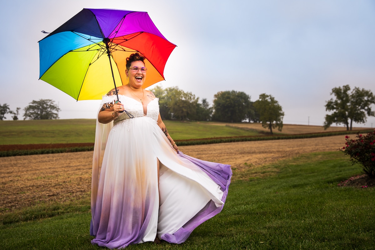 unique, colorful, vibrant image of farm land in the background and the bride in her colorful creative unique dress holding their rainbow umbrella during their preparation photos 