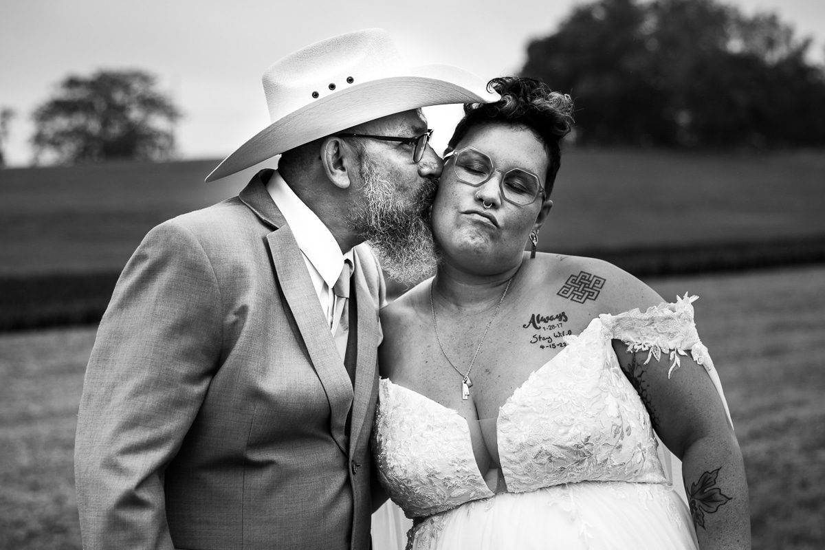 Black and white image of their father in a cowboy hat giving a kiss to them on their cheek during their preparation photos in Waynesboro pa 