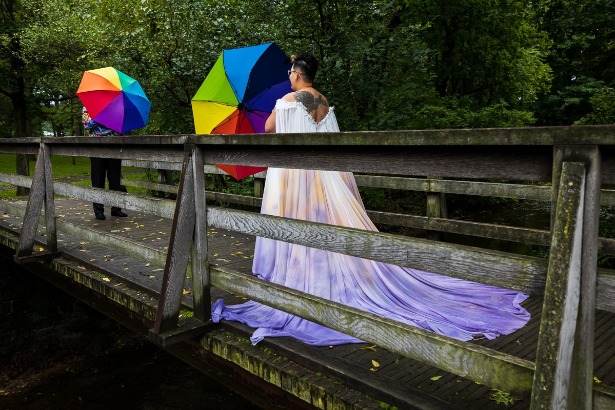 Pennsylvania LGBTQIA+ Photographer, Rhinehart Photography captured this image of the couple right before their first look of them holding their rainbow umbrellas in front of their faces on a bridge in Renfrew Park, Waynesboro, PA