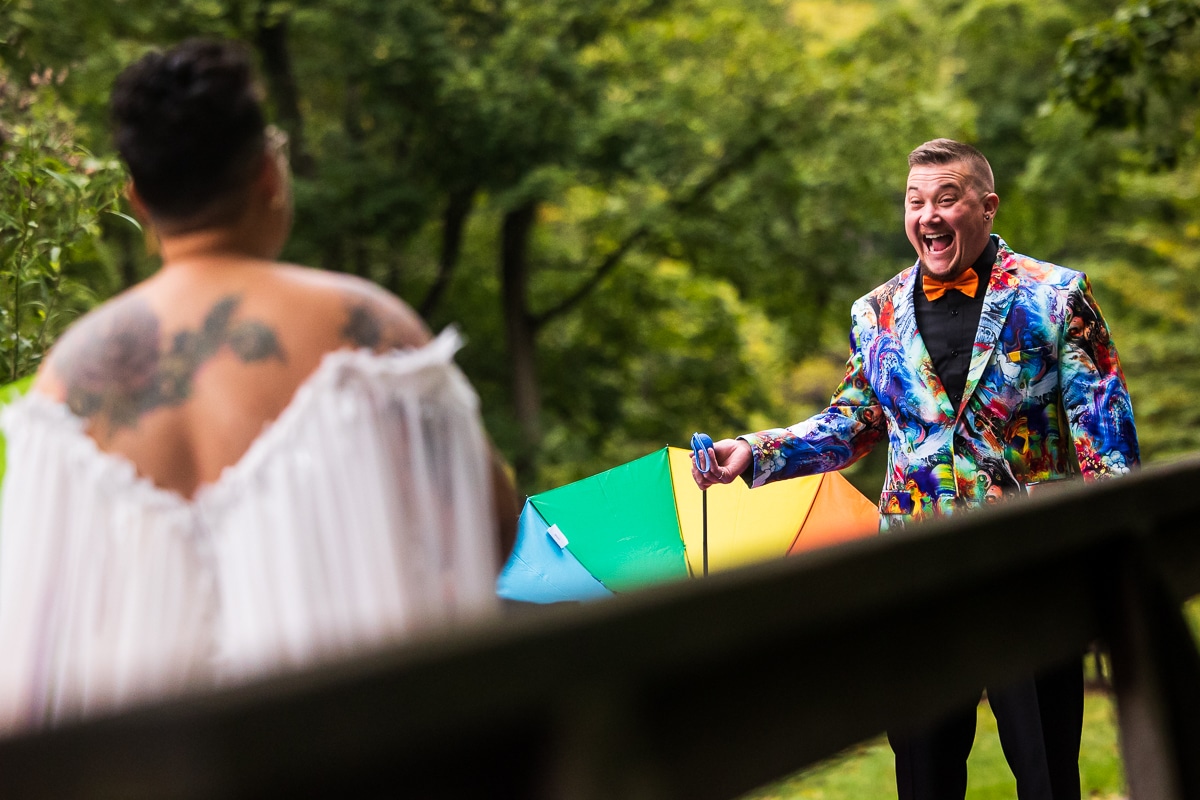 LGBTQIA+ Wedding Photographer, Lisa Rhinehart captured this couples colorful and vibrant first look of the groom shocked as he holding his rainbow umbrella in his unique, creative, colorful tux