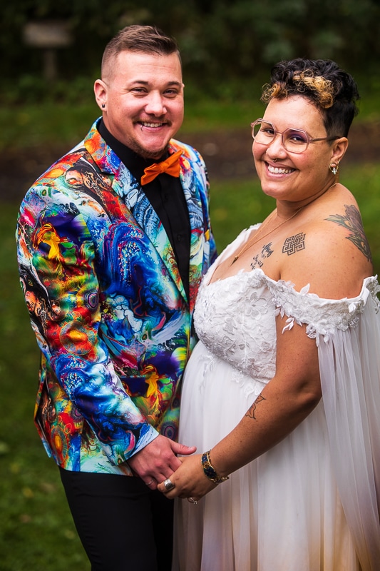 traditional portrait of this queer and trans couple holding hands and smiling towards best pa wedding photographer, Lisa Rhinehart, before their backyard wedding in waynesboro, pa