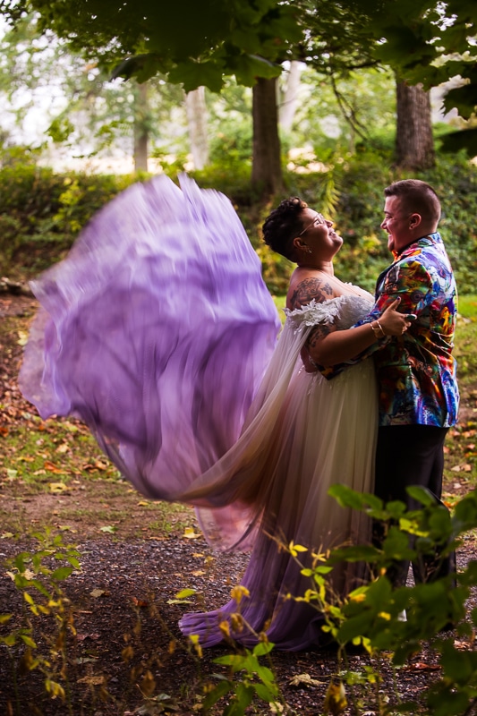 Best PA wedding photographer, Lisa Rhinehart, captured this Unqiue, colorful, vibrant image of this queer and trans couple in their colorful wedding attire with the purple dress flying in the wind before their backyard wedding in pa