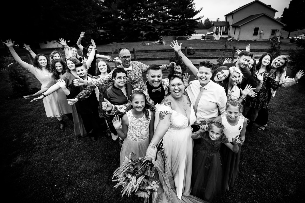 PA wedding photographer, lisa rhinehart, captures this black and white image of the bridal party with their arms and hands in the air and all smiles towards the camera. the bridal party is in a similar shape as a heart 
