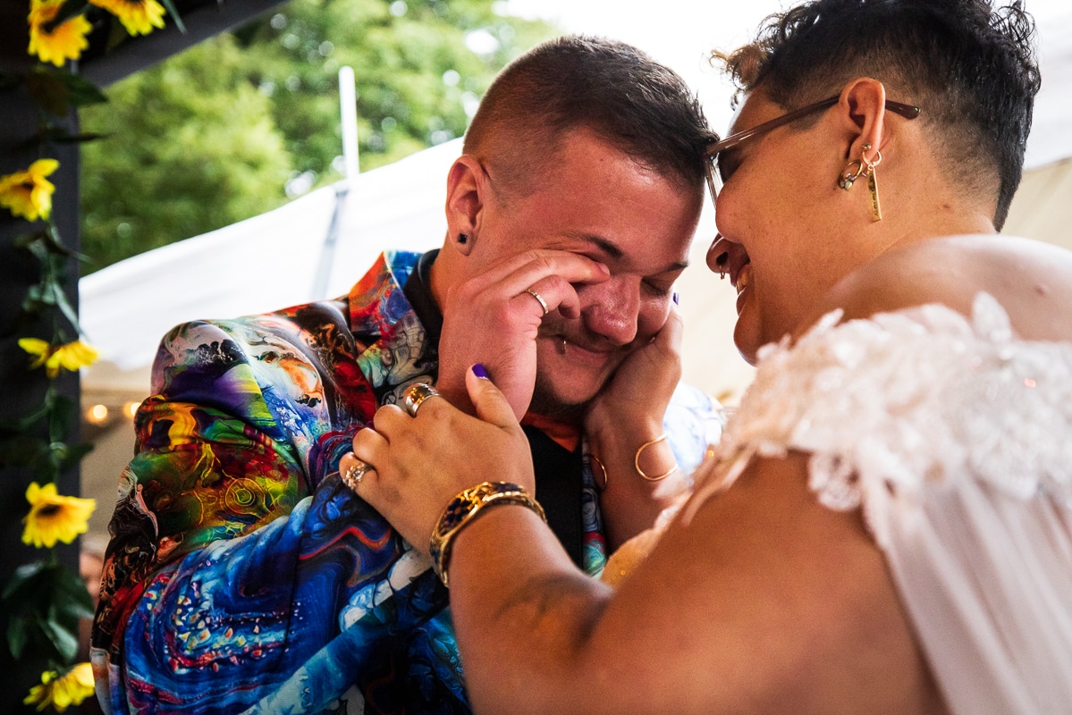LGBTQIA+ Wedding Photographer, Lisa Rhinehart captured this queer and trans couples during their backyard wedding ceremony laughing and crying with one another in their unique and colorful wedding attire