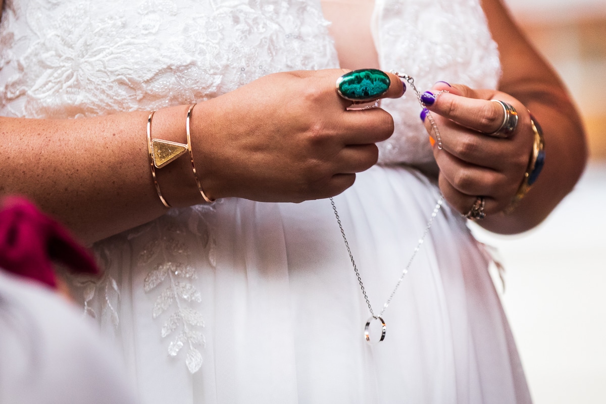 image of the ring for the groom on a necklace with the bride's colorful fingernails and lots of colorful and unique jewelry on her wrists and fingers during their outdoor wedding ceremony