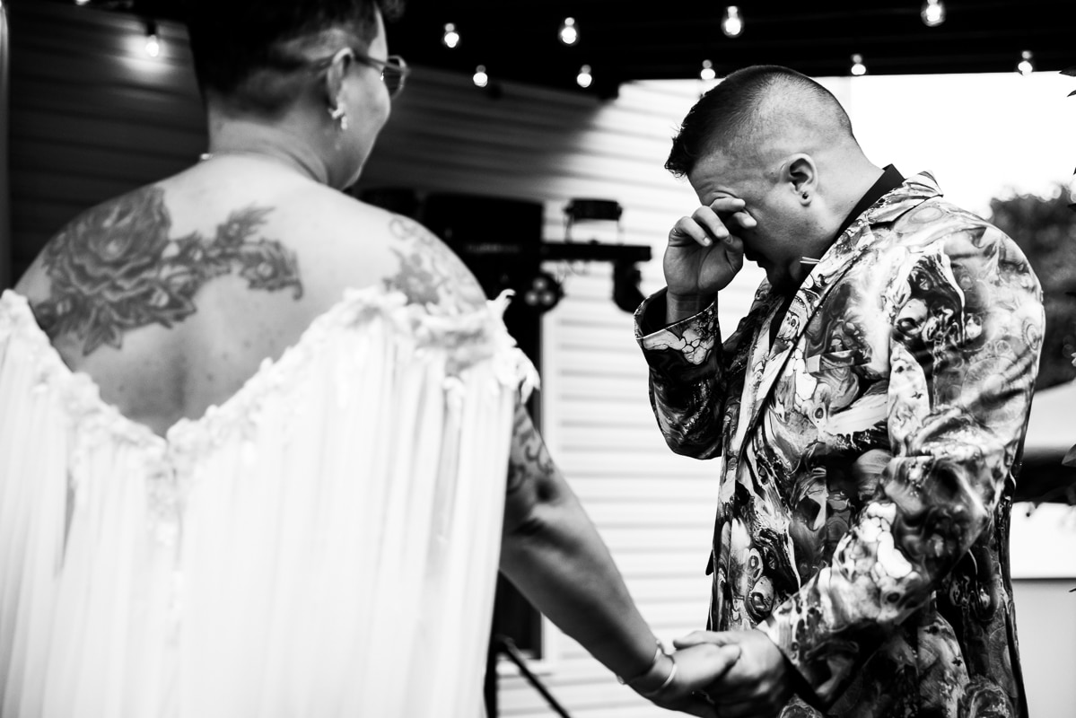 LGBTQIA+ Wedding Photographer, Lisa Rhinehart captures the groom wiping away tears from his eyes during their wedding ceremony near Renfrew Park, Waynesboro, PA