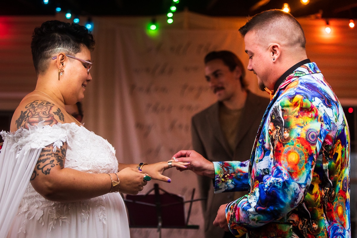 Best PA Wedding photographer, lisa rhinehart, captures the couple exchanging their rings and placing them on one another's fingers in their colorful, creative and unique wedding attire during their backyard wedding ceremony in Pennsylvania