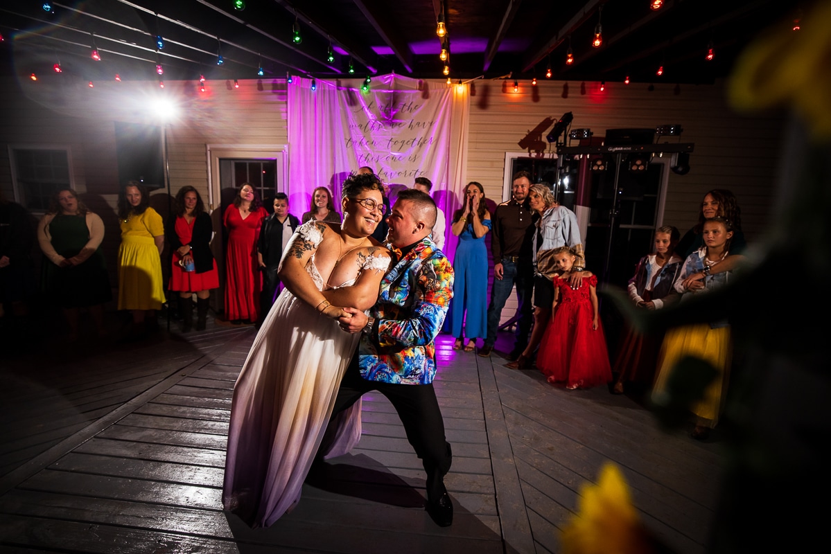 LGBTQIA+ Wedding Photographer, Lisa Rhinehart captures the couple dancing together as their guests watching in the background behind them from the deck in their backyard wedding 