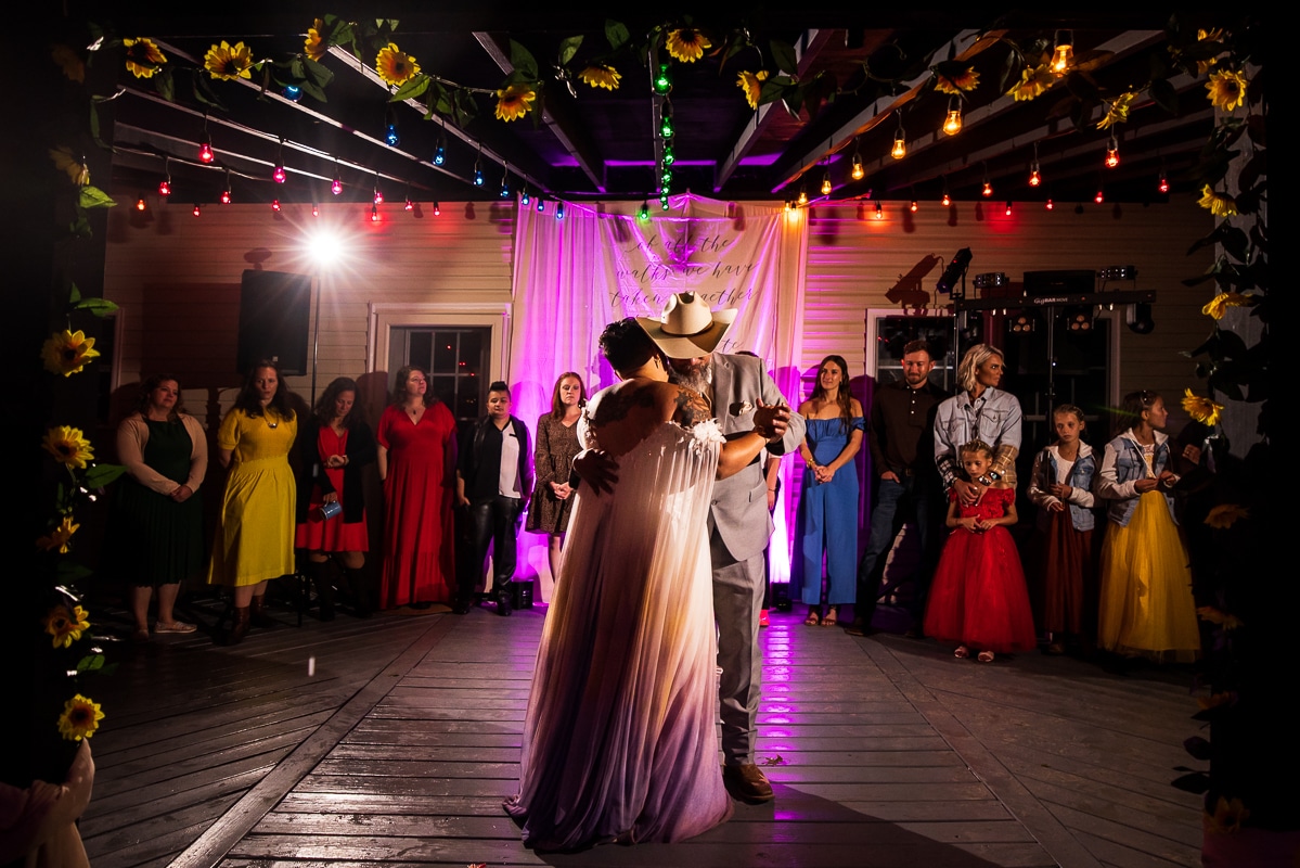 Backyard wedding photographer, Rhinehart Photography, captures the parent and family dances from the night as family and friends watch from behind as colorful lights and sunflower decorations fill the space