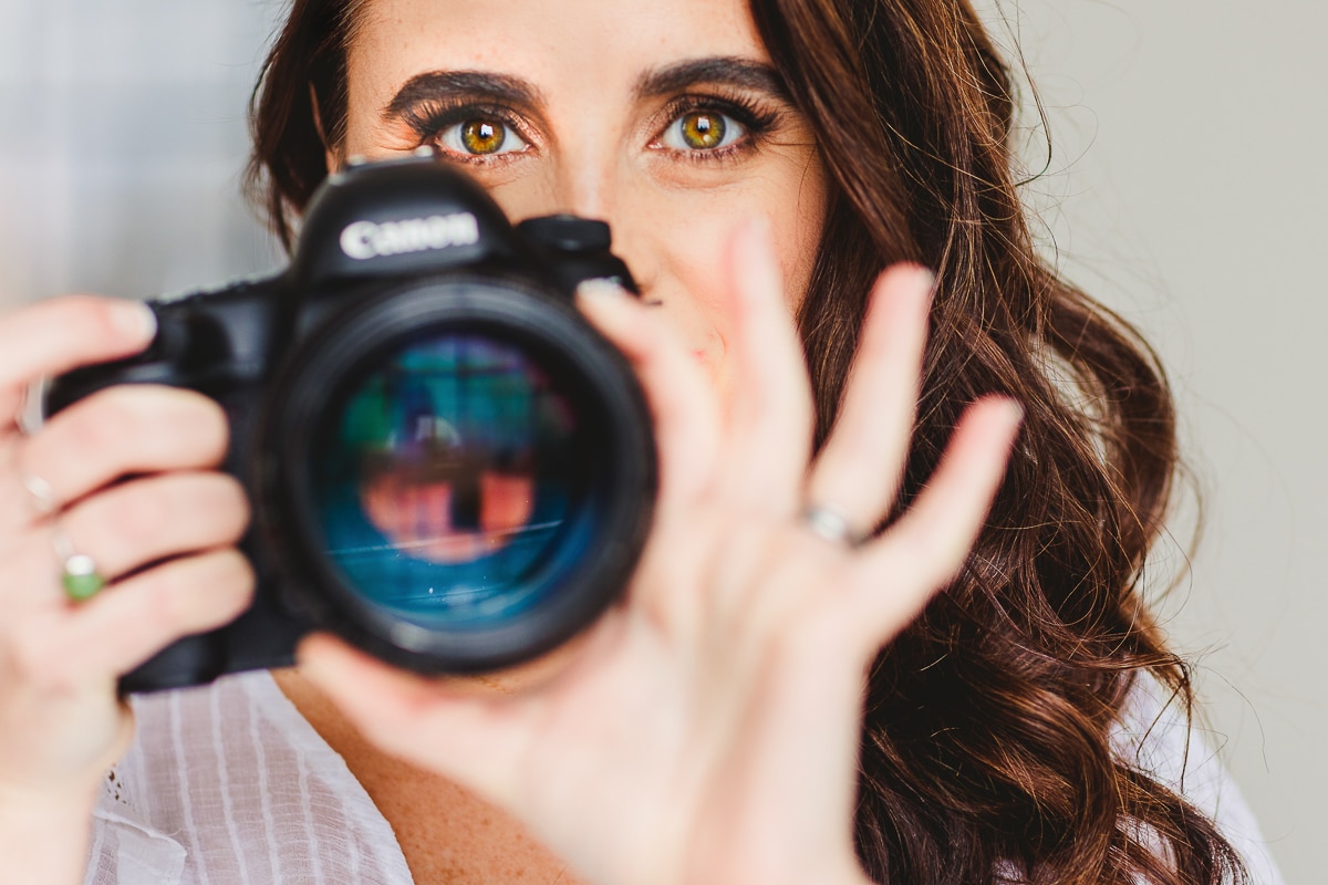 Lisa Rhinehart award winning creative candid wedding photographer serving pennsylvania pa washington dc dc asnd beyond holding a canon camera with a white background and just her eyes showing