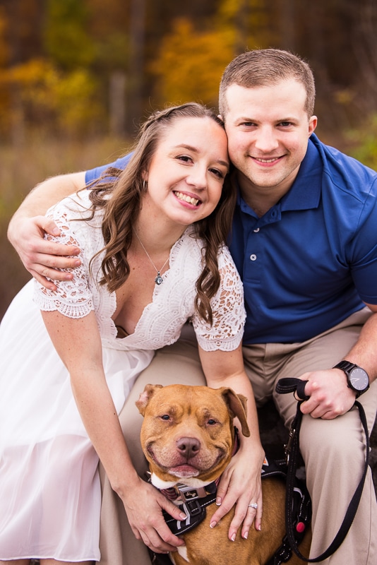 Image of the couple smiling and holding their dog as their dog smiles at the camera too during this dog engagement session
