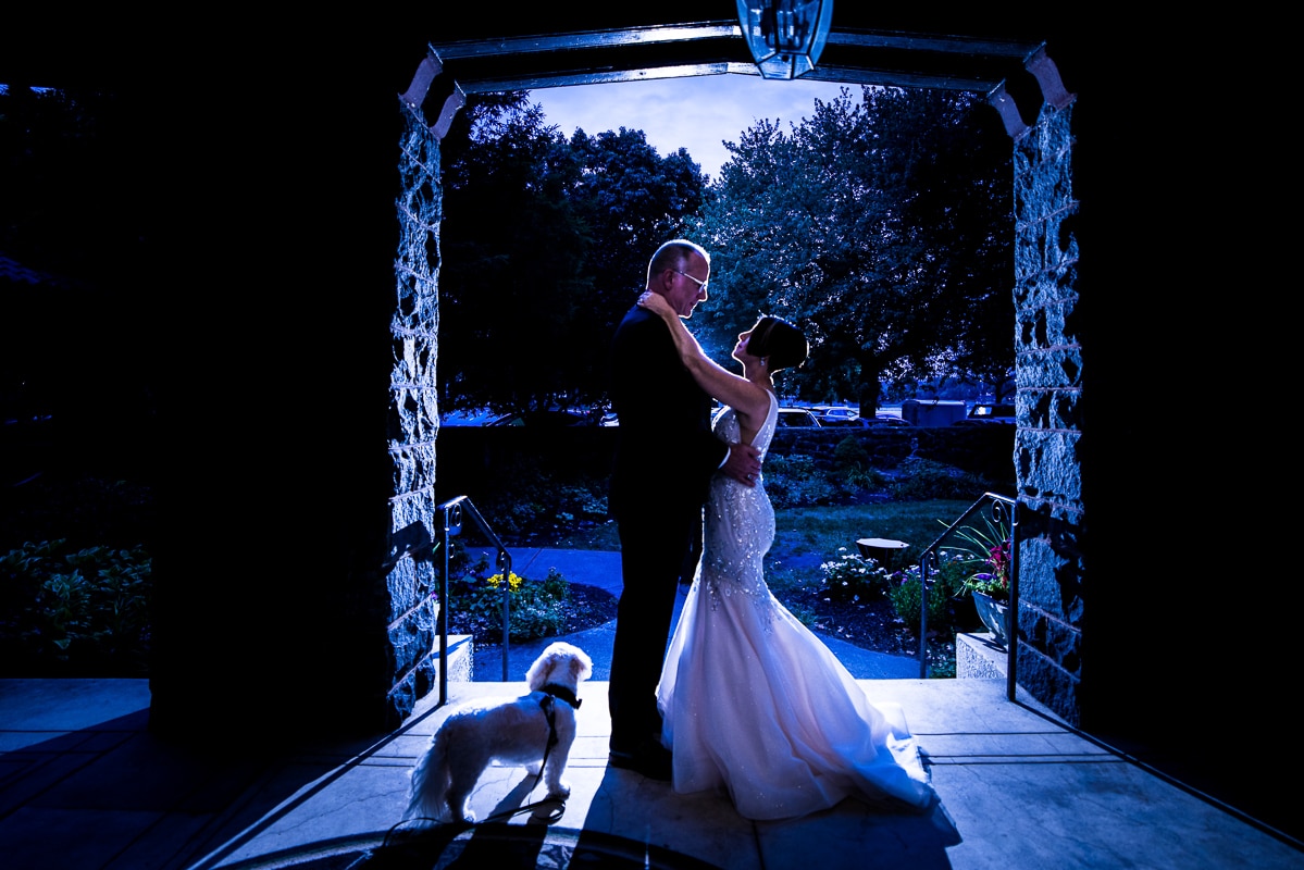 Blue toned photo of the bride and groom standing in an arch way for their Harrisburg Civic Club wedding with their dog beside them