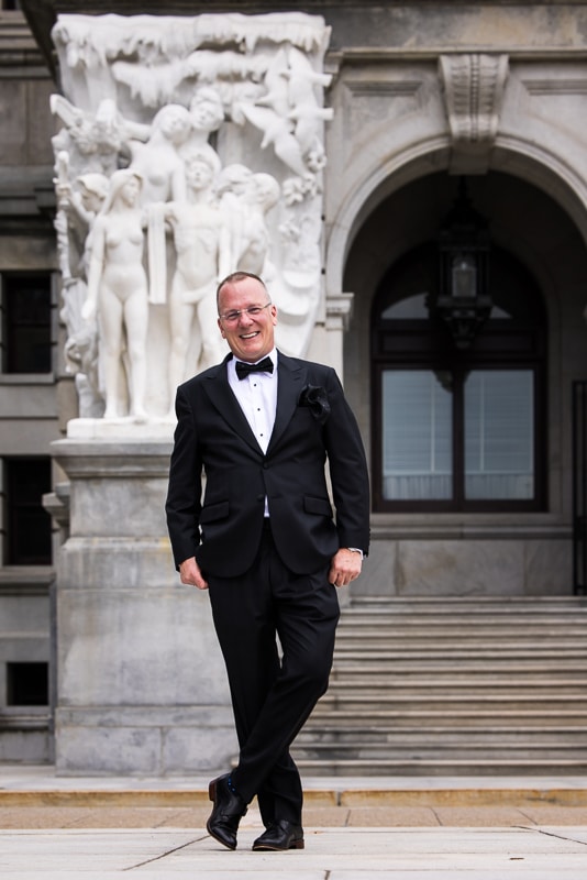 Traditional photo of the groom standing outside posing in his black tux before the wedding ceremony, this photo was taken by Lisa Rhinehart a Harrisburg wedding photographer