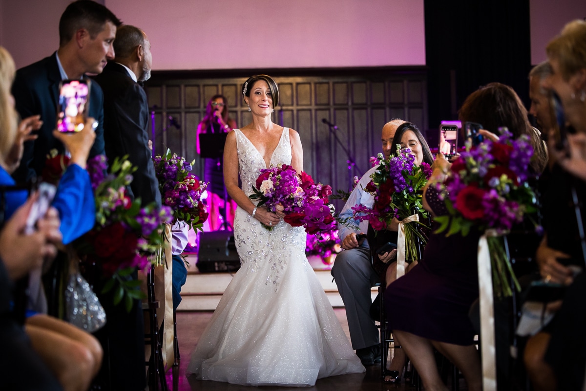 Colorful photo of the bride walking down the aisle during her Harrisburg civic club wedding ceremony holding her vibrant bouquet