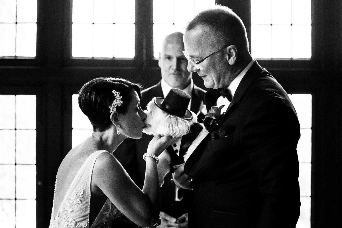 Black and white photo of the groom holding the dog while the bride kisses the dog during their Harrisburg civic club wedding ceremony