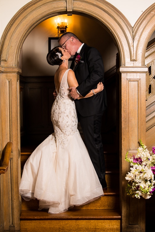 Bride and groom standing inside in an wood arch way kissing on another 