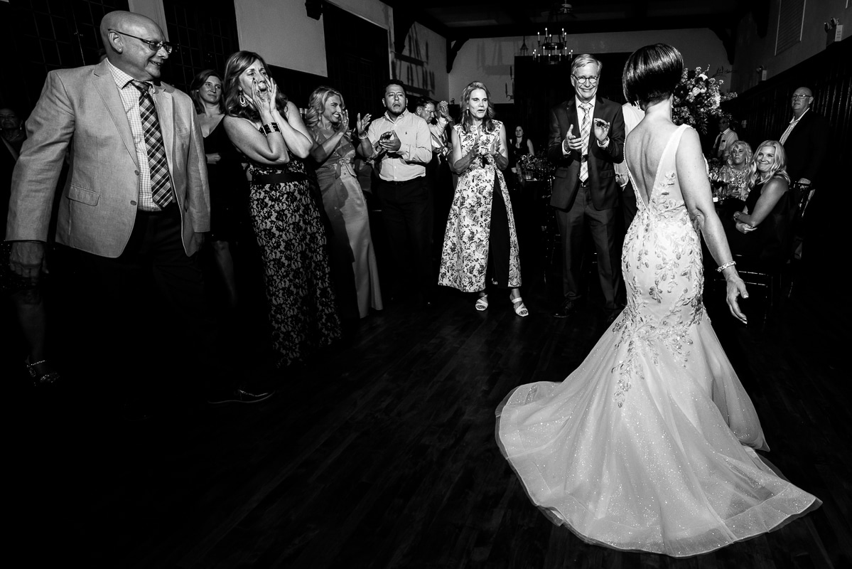 black and white image of the bride showing off her dress to guests as they cheer and lap for her 