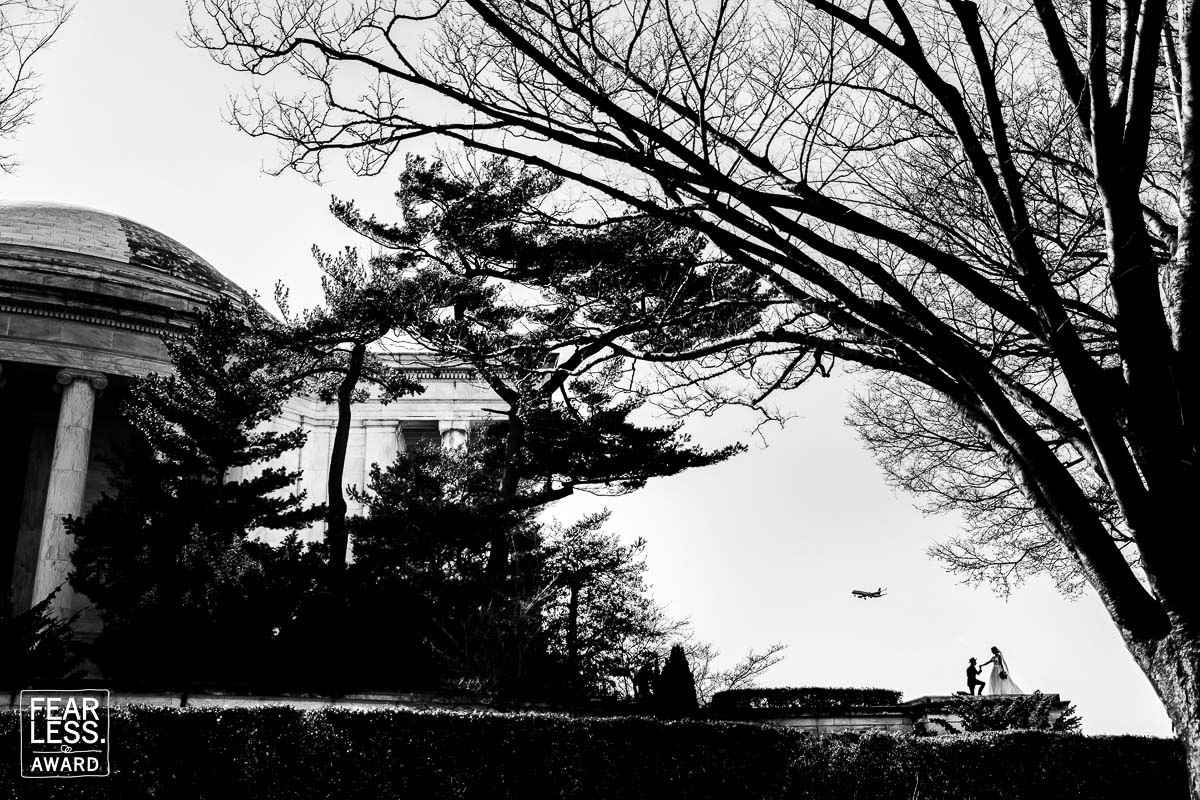 black and white image from fearless photographer, Lisa Rhinehart, capturing the bride and groom in the bottom corner with a plane flying over them