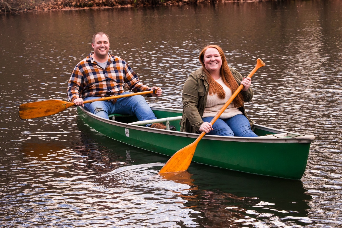unique, fun engagement photo of the couple smiling towards the camera as the paddle around the pond in a green canoe during their engagement session