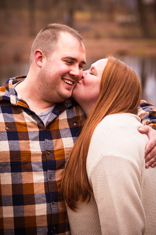 image of the couple kissing one another on the cheek during their engagement session in pennsylvania
