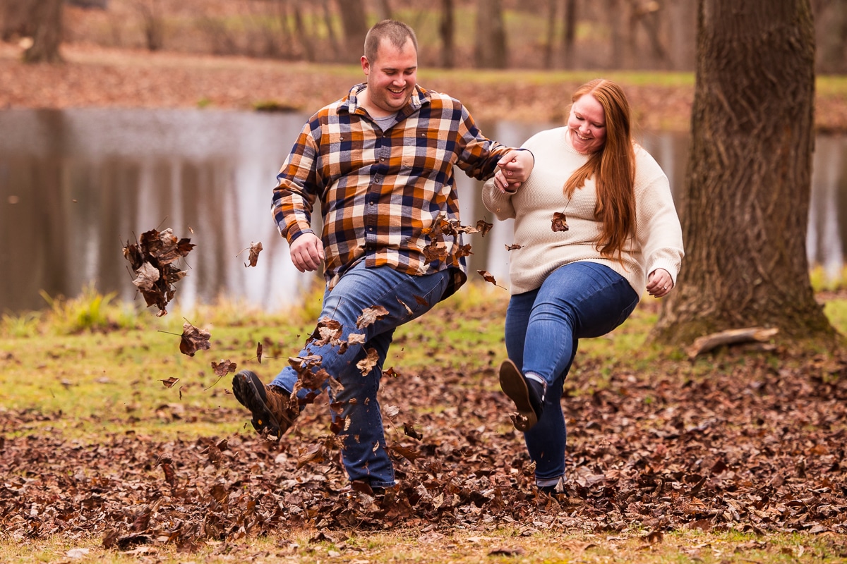 unique, fun image of the couple holding hands and kicking a pile of leaves together during their outdoor fall engagement session in central pa 