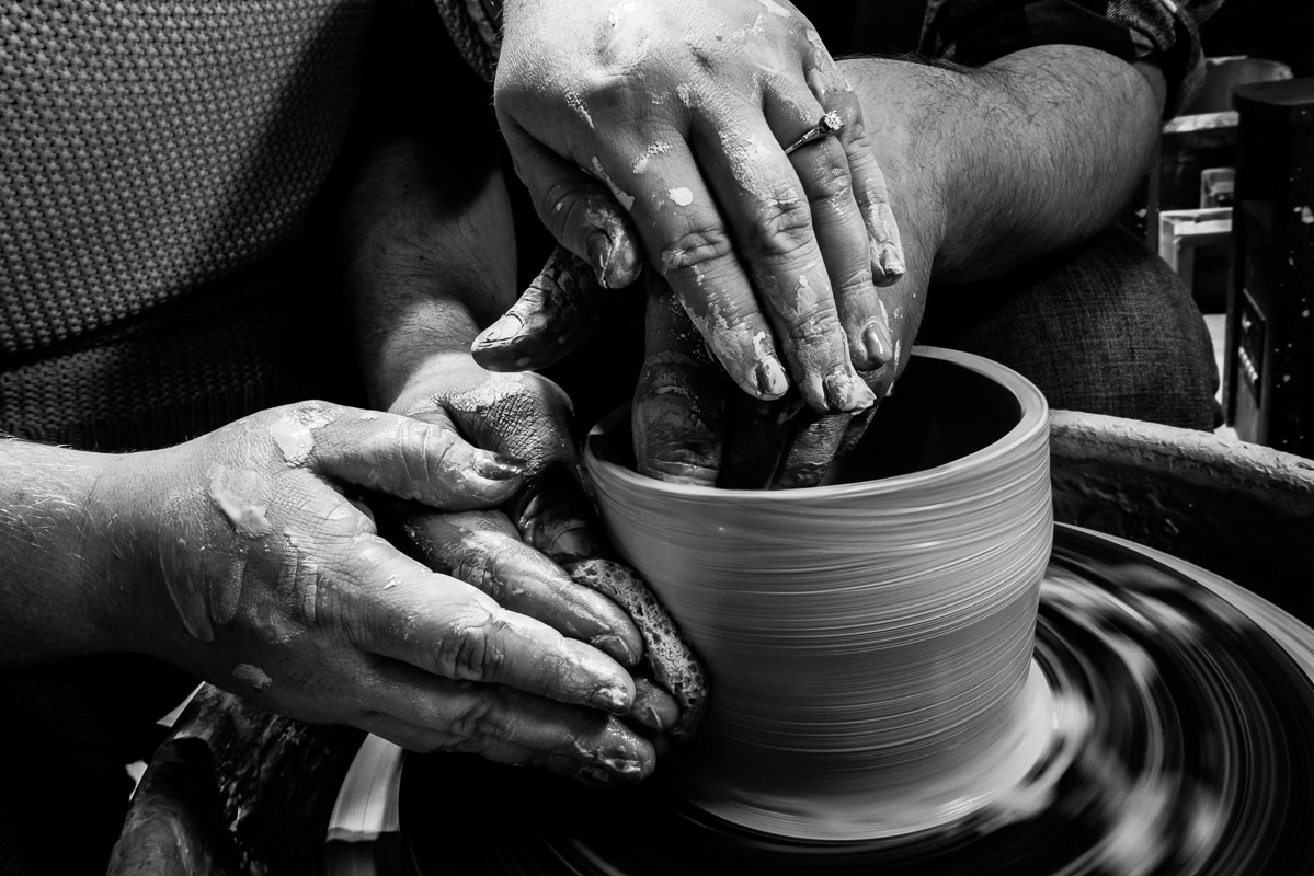 Up close black and white image of the couple clay covered hands as they make pottery together on a pottery wheel during the central pa engagement session